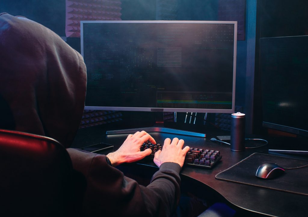 A man in a hood typing on a desktop computer