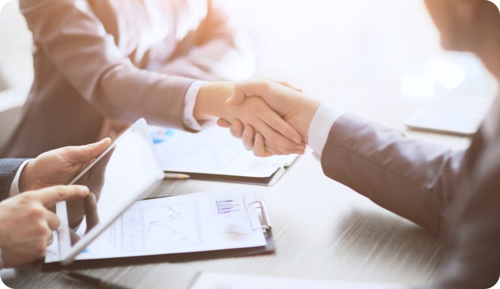 Two people shaking hands over a desk with work materials on it