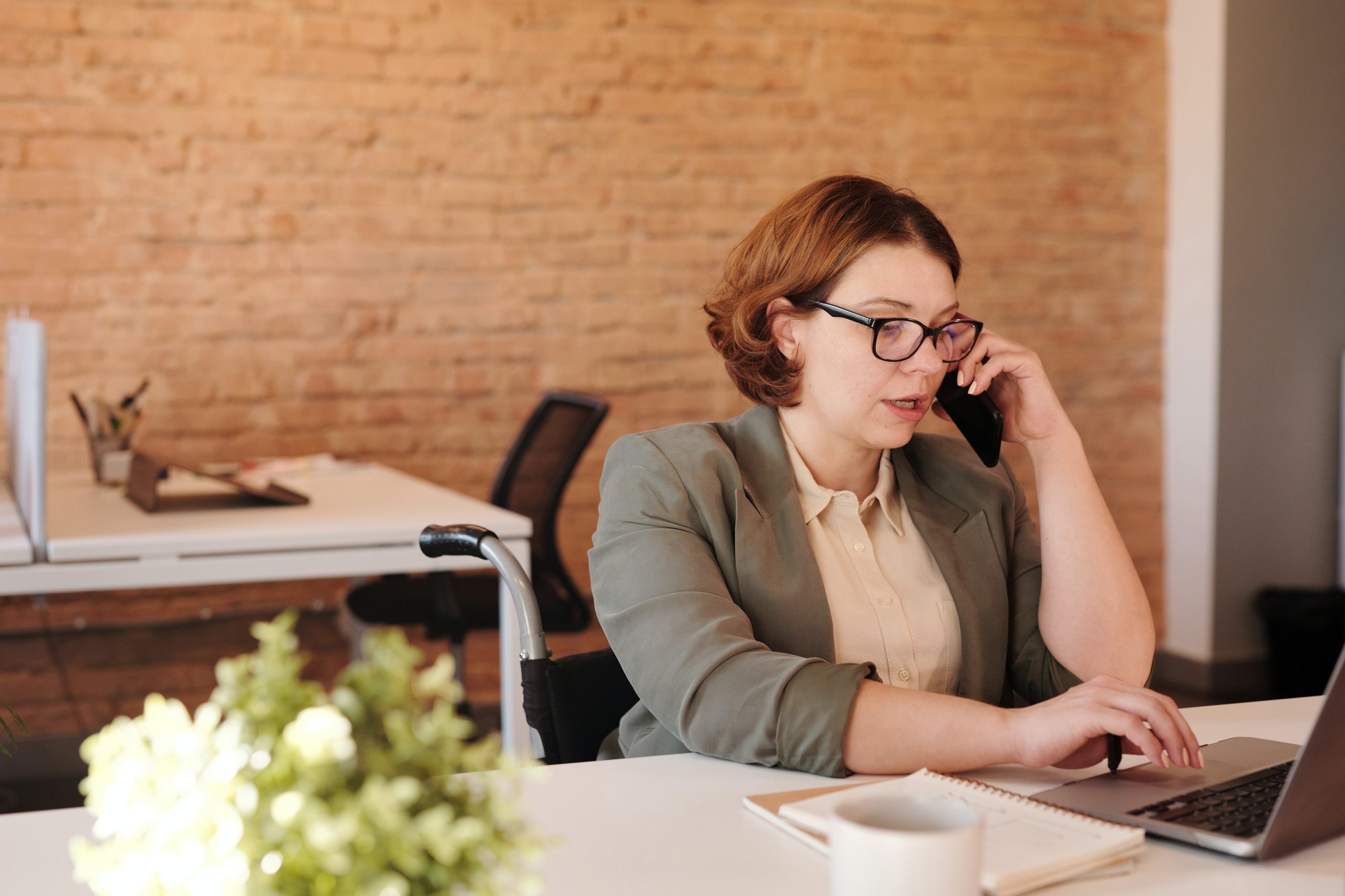 A woman talking on a phone and working on a laptop